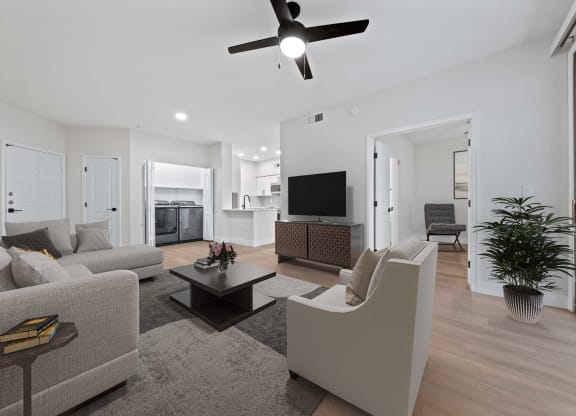 a living room with couches and a kitchen and a ceiling fan